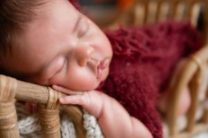 Baby sleeping peacefully on wooden surface with burgundy textured blanket.