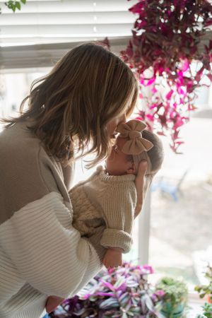 Tender moment between parent and baby near window with pink flowers in background.