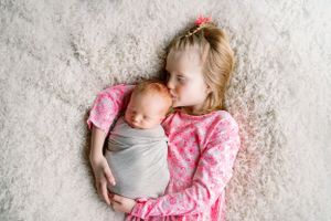 Siblings in pink and gray sharing a tender moment on plush carpet.