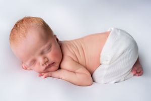 Peaceful newborn baby sleeping in white diaper against light background.