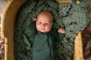 Baby sleeping peacefully in circular wicker basket with sage green bedding.