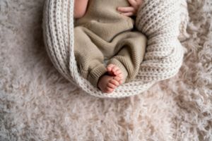 Tiny baby feet peeking out from cozy knit blanket and sweater.