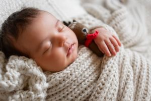 Baby wrapped in chunky knit cream blanket during newborn photo session.