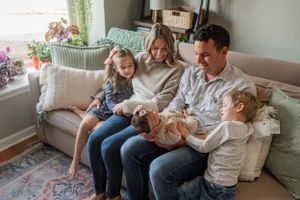 Happy family relaxing together on a cozy gray couch with decorative pillows and plants.