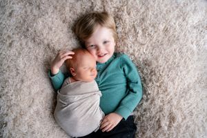 Siblings cuddling on carpet with older child in teal sweater.