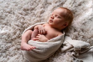Peaceful sleeping newborn wrapped in soft white blanket on textured carpet.
