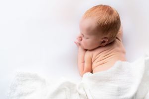 Side view of sleeping newborn wrapped in soft white fabric.