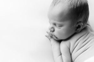Black and white close-up of sleeping infant resting on arm.