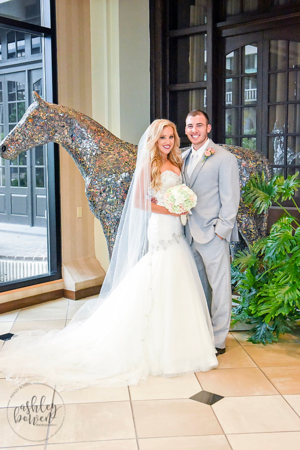 Bride and groom posing beside a glittering mosaic horse sculpture in elegant wedding venue.