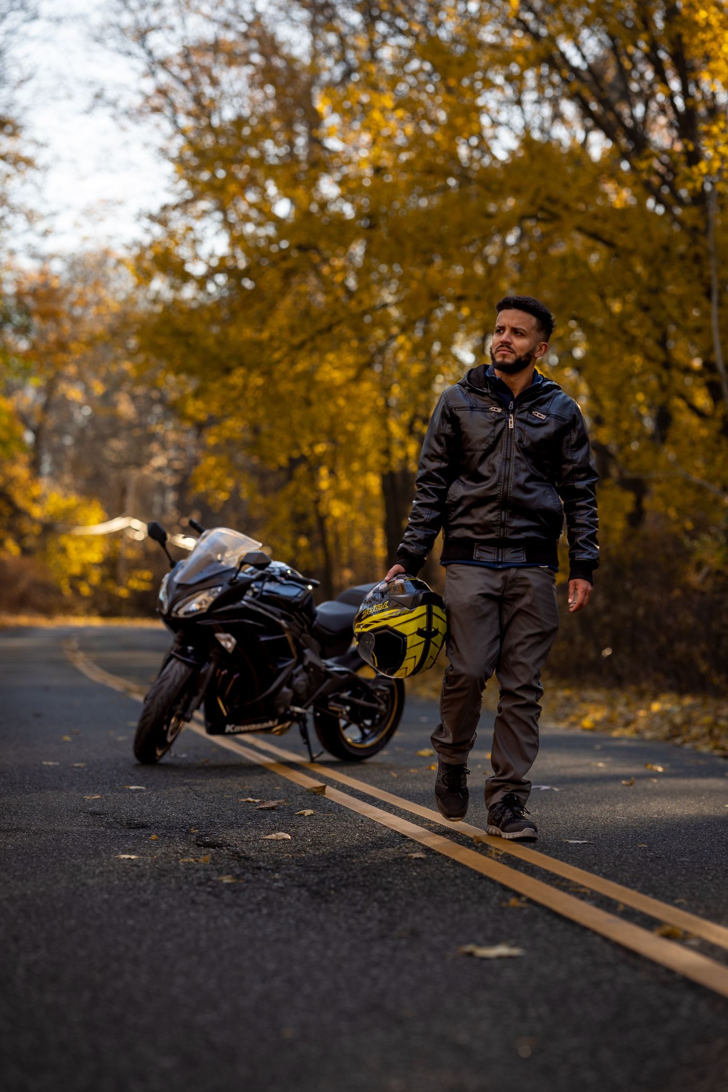 Motorcyclist standing beside sport bike on autumn road with golden foliage.