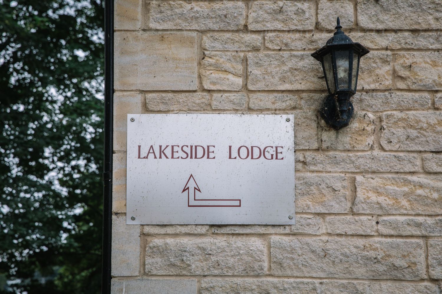 A stone wall with a directional sign reading 'Lakeside Lodge' and a mounted black lantern fixture.