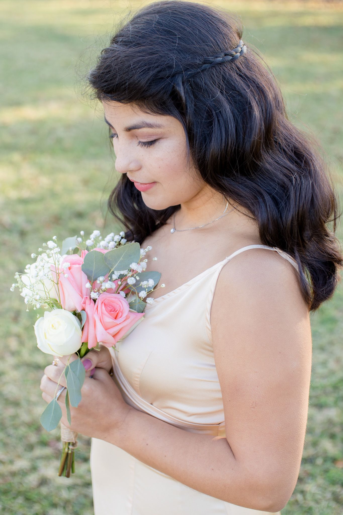 Person in cream colored top holds a delicate bouquet of pink and white roses in an outdoor setting.