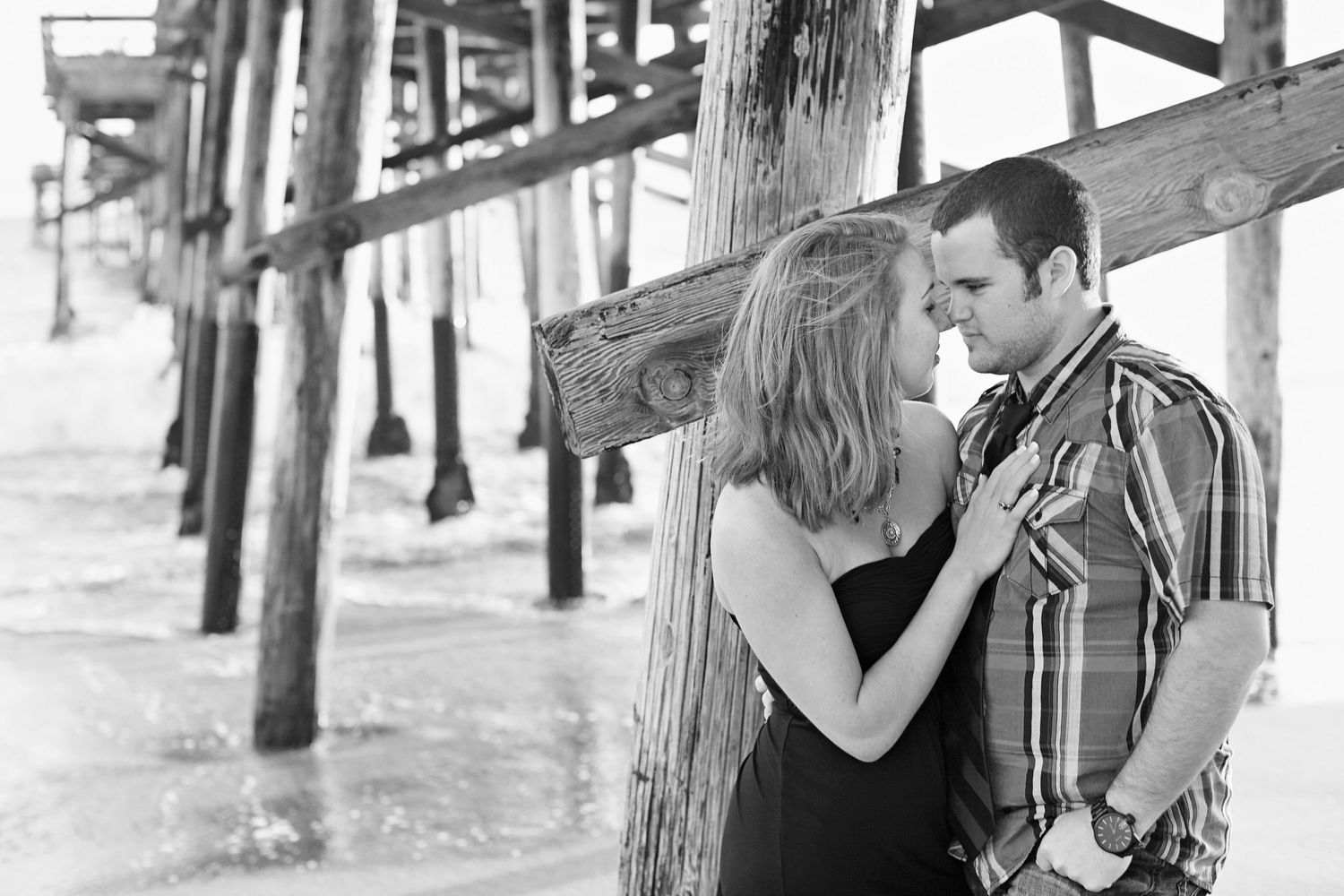 Couple in casual clothes sharing an intimate moment by wooden pier posts in black and white.