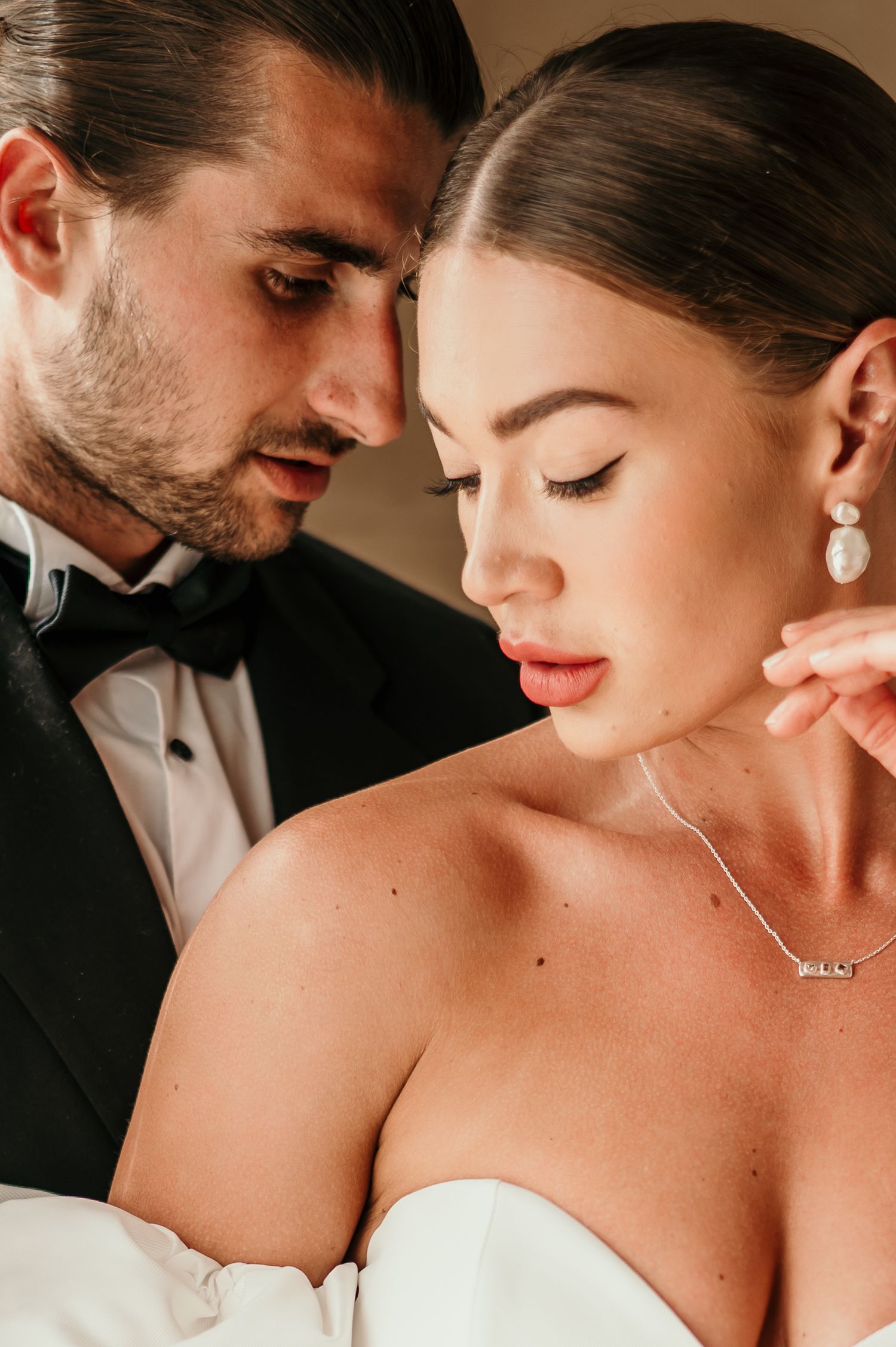 Romantic close-up portrait of couple in formal wedding attire with soft lighting and elegant jewelry.