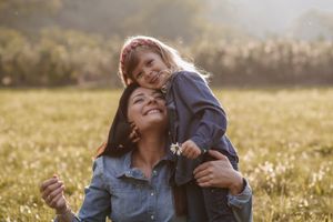 Mother and child share loving moment in summer wildflower field at sunset.