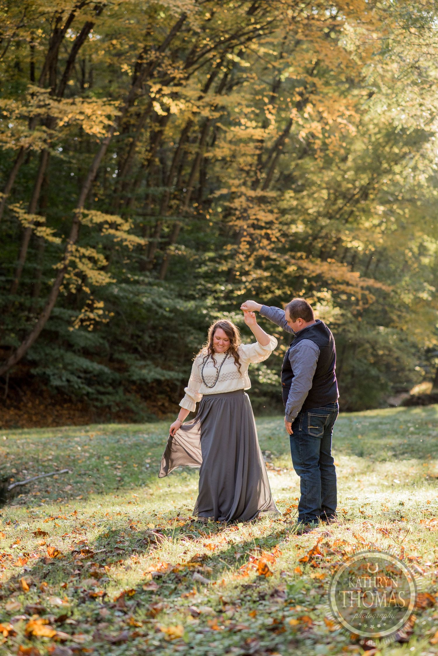 A couple dances playfully in a sunny autumn forest clearing surrounded by fall foliage.