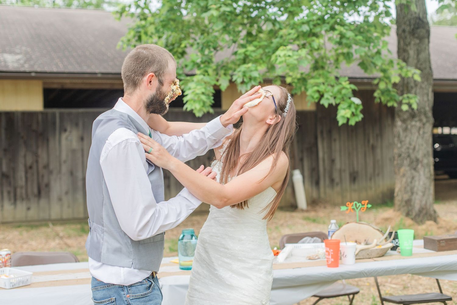 Wedding couple shares intimate moments during outdoor reception under trees.