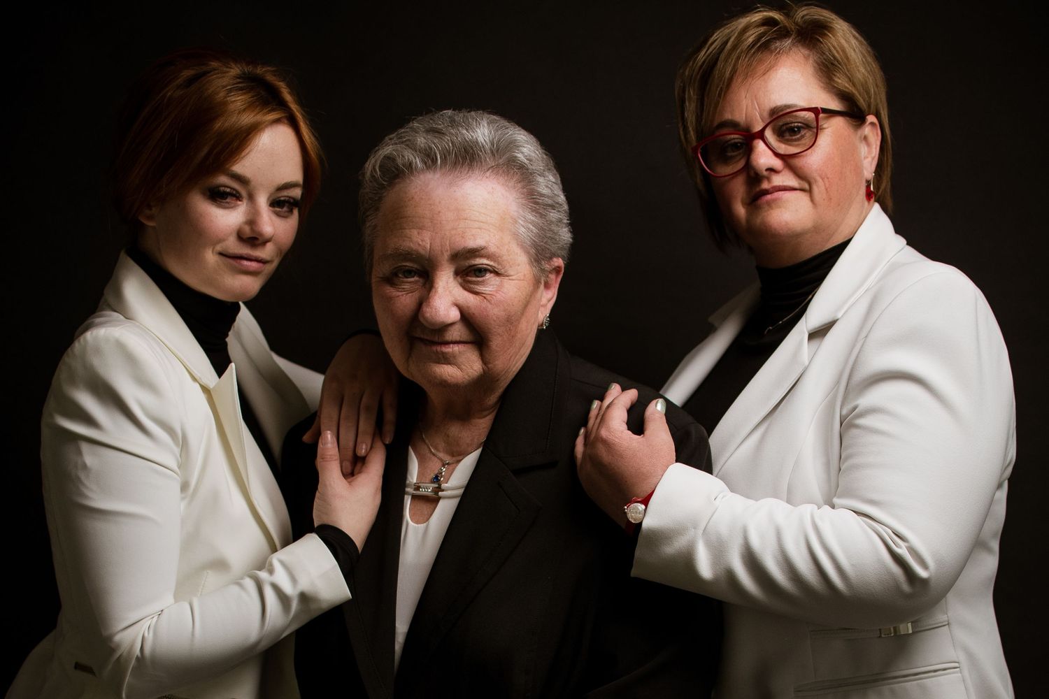 Professional studio portrait of three generations in white and black formal attire.