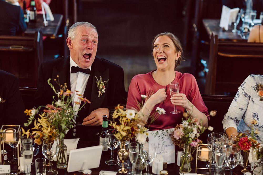 Wedding reception guests laughing and celebrating at decorated dining tables.