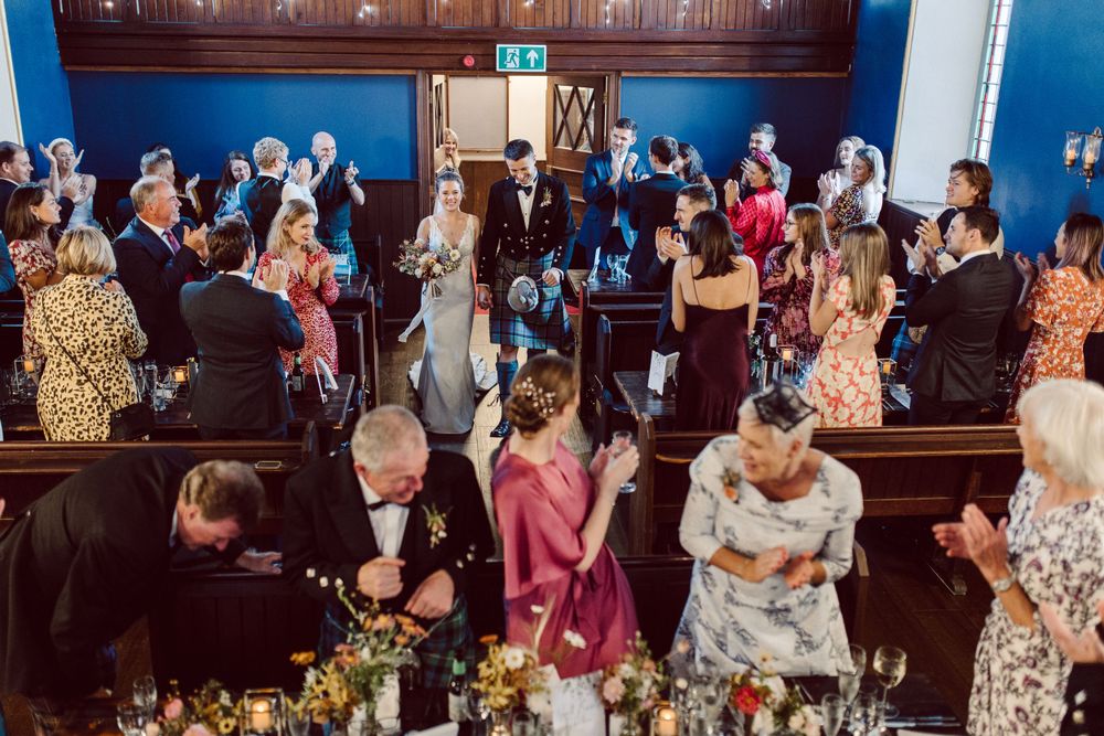 Wedding guests seated at long tables in an elegant blue-walled reception venue.