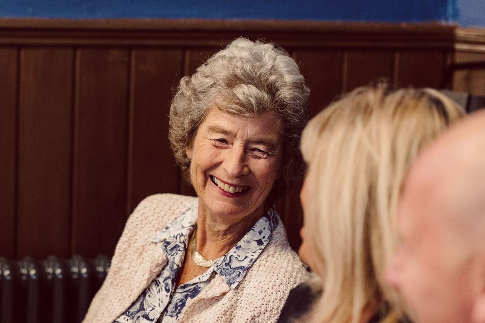 Wedding guests enjoying a formal reception in an elegant blue-walled dining room with stained glass windows.