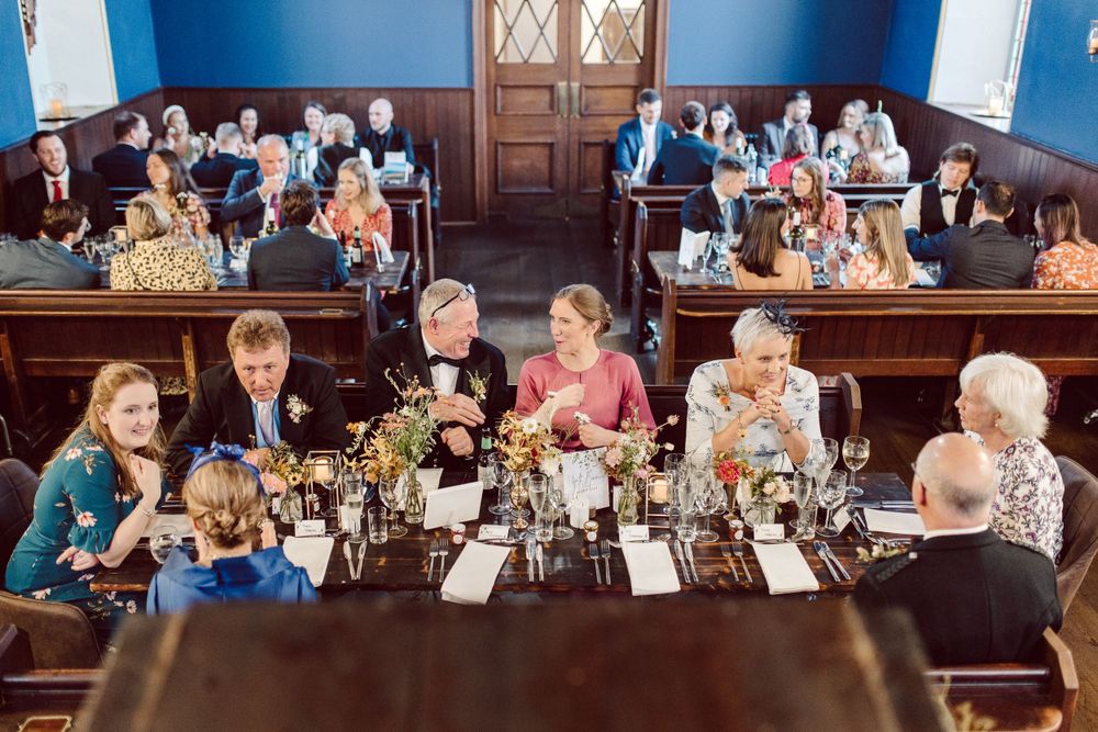 Large wedding reception hall with blue walls and wooden details filled with celebrating guests.