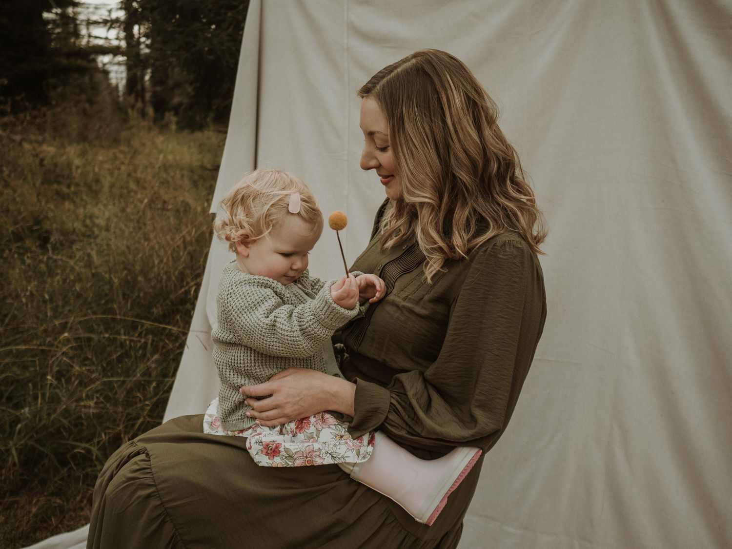 Mother with toddler daughter sitting together outside with a flower