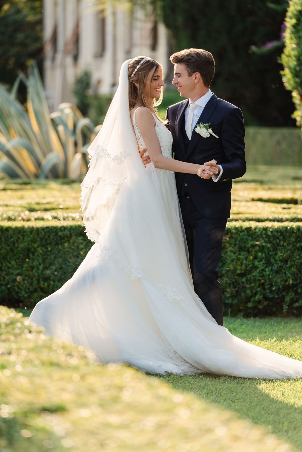 Newlyweds dance together on manicured garden lawn in golden sunlight.