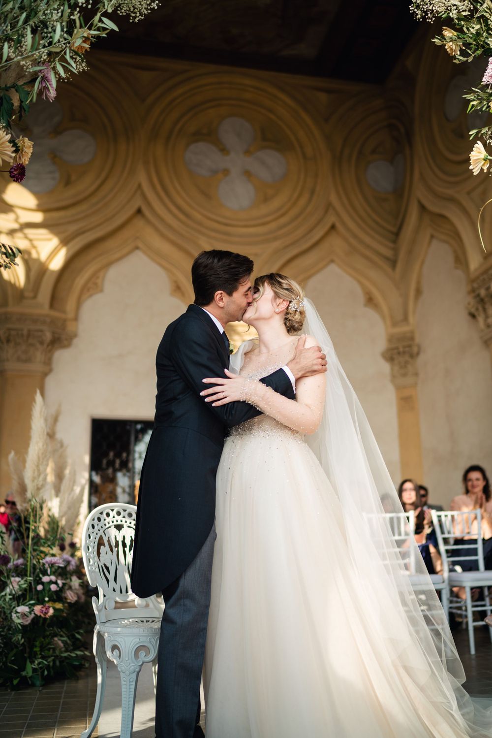 Romantic wedding moment under ornate stone arches decorated with flowers.