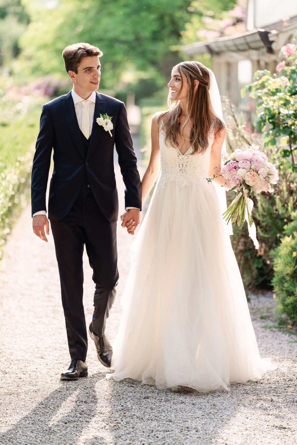 Couple walking hand in hand down a garden path in formal wedding attire.