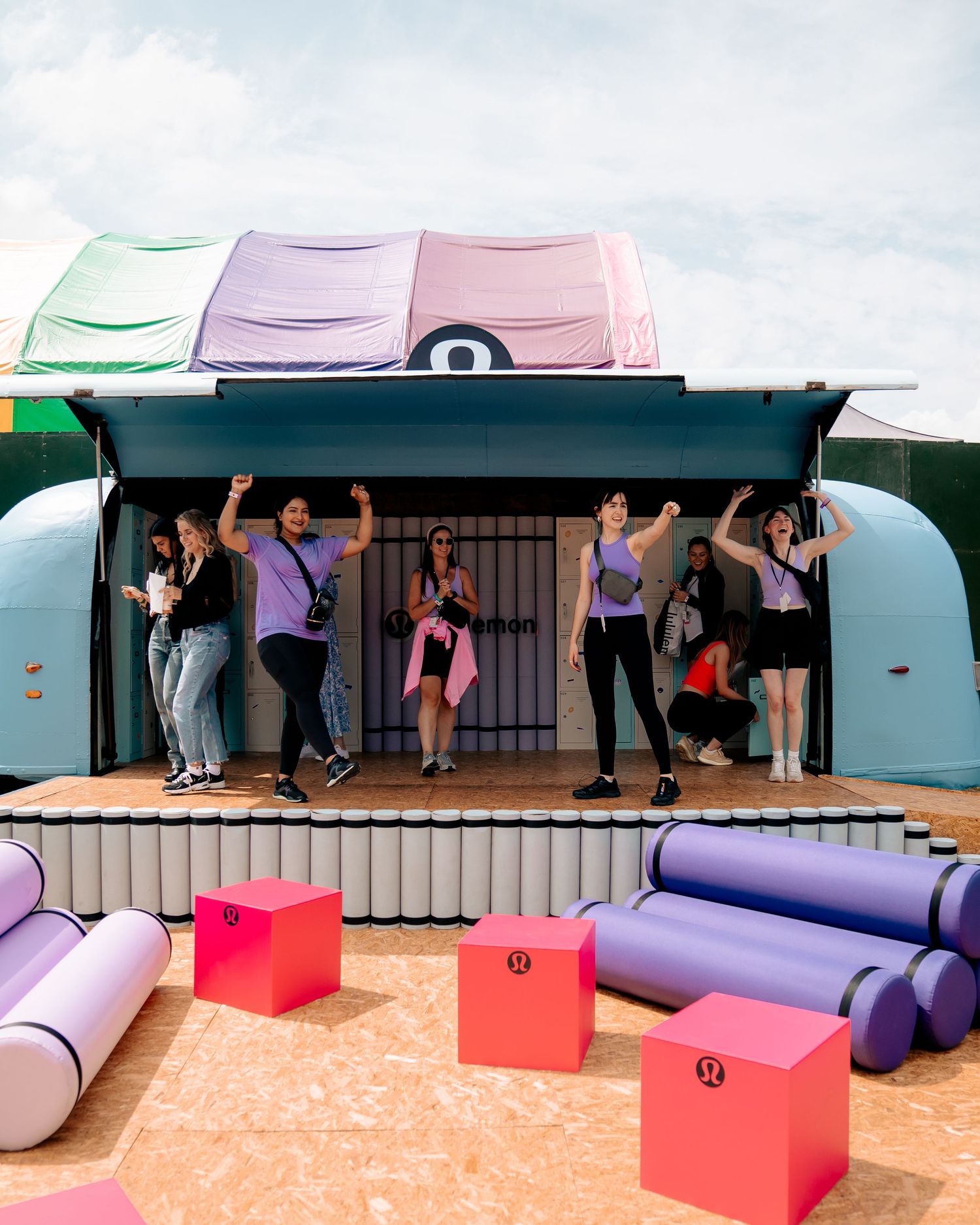 Group fitness class participants jumping and exercising on an outdoor platform with purple equipment.