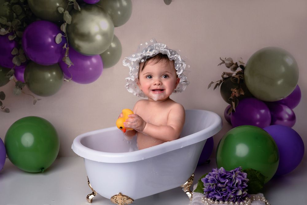 One-year-old girl with a balloons backdrop smiling during first birthday photo shoot Bath Splash