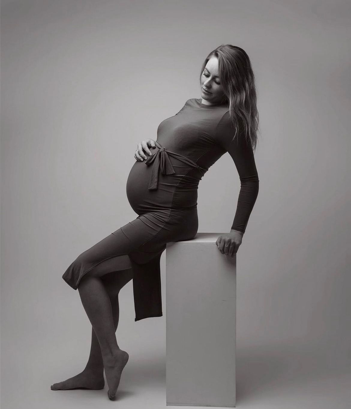 Kunstnerisk sort-hvid graviditetsfotoshoot med positurer og en minimalistisk hvid kube som rekvisit.