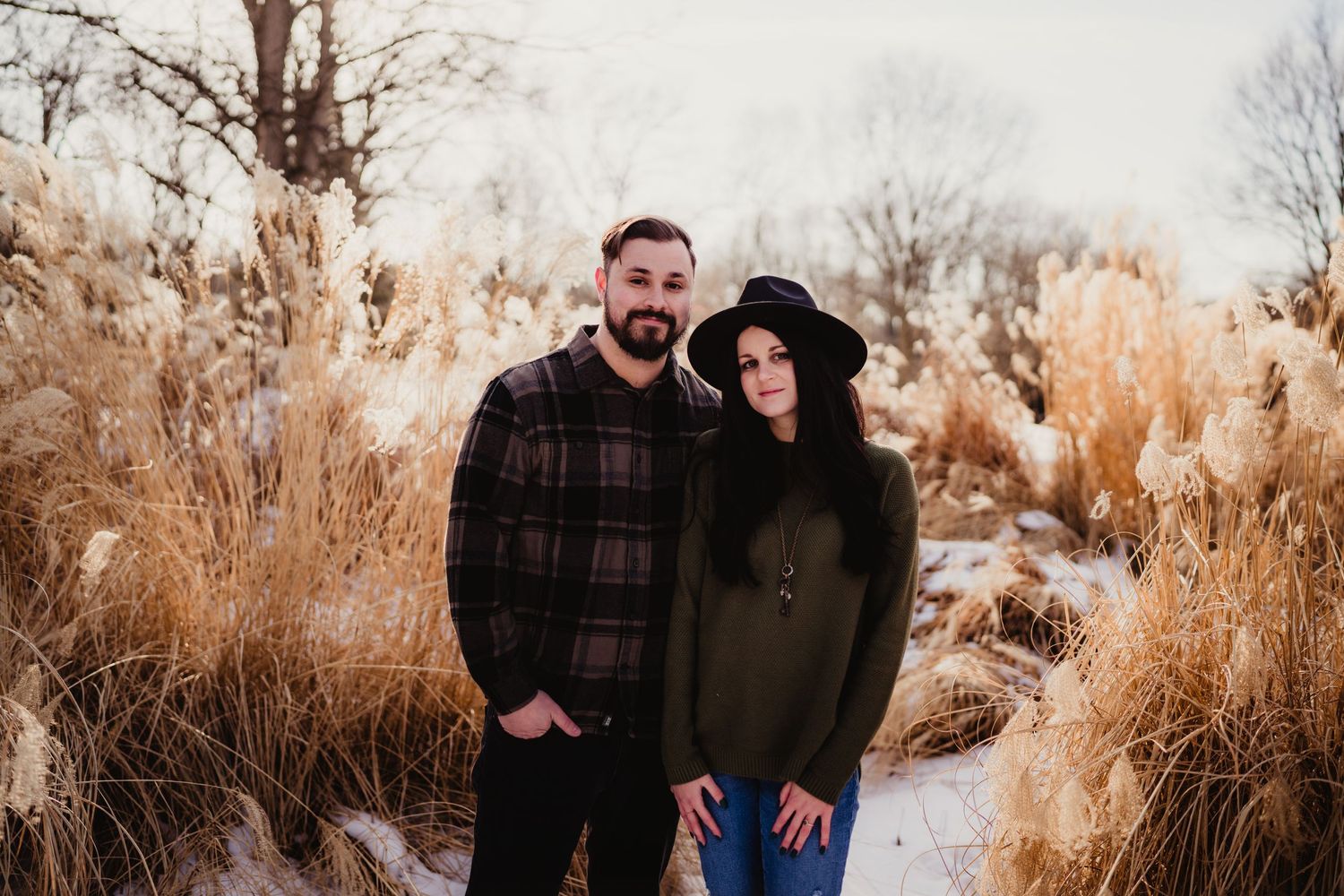 Winter portrait of a couple standing among dried grass with one person wearing a black hat.