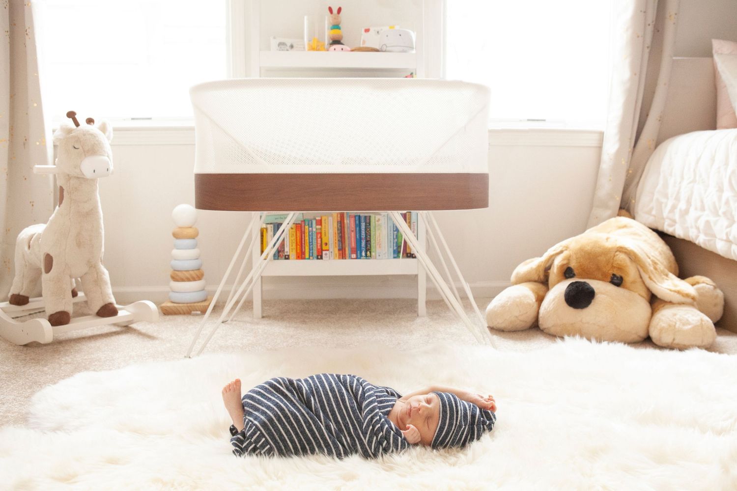 A nursery room with stuffed animals and a sleeping baby on a white rug.