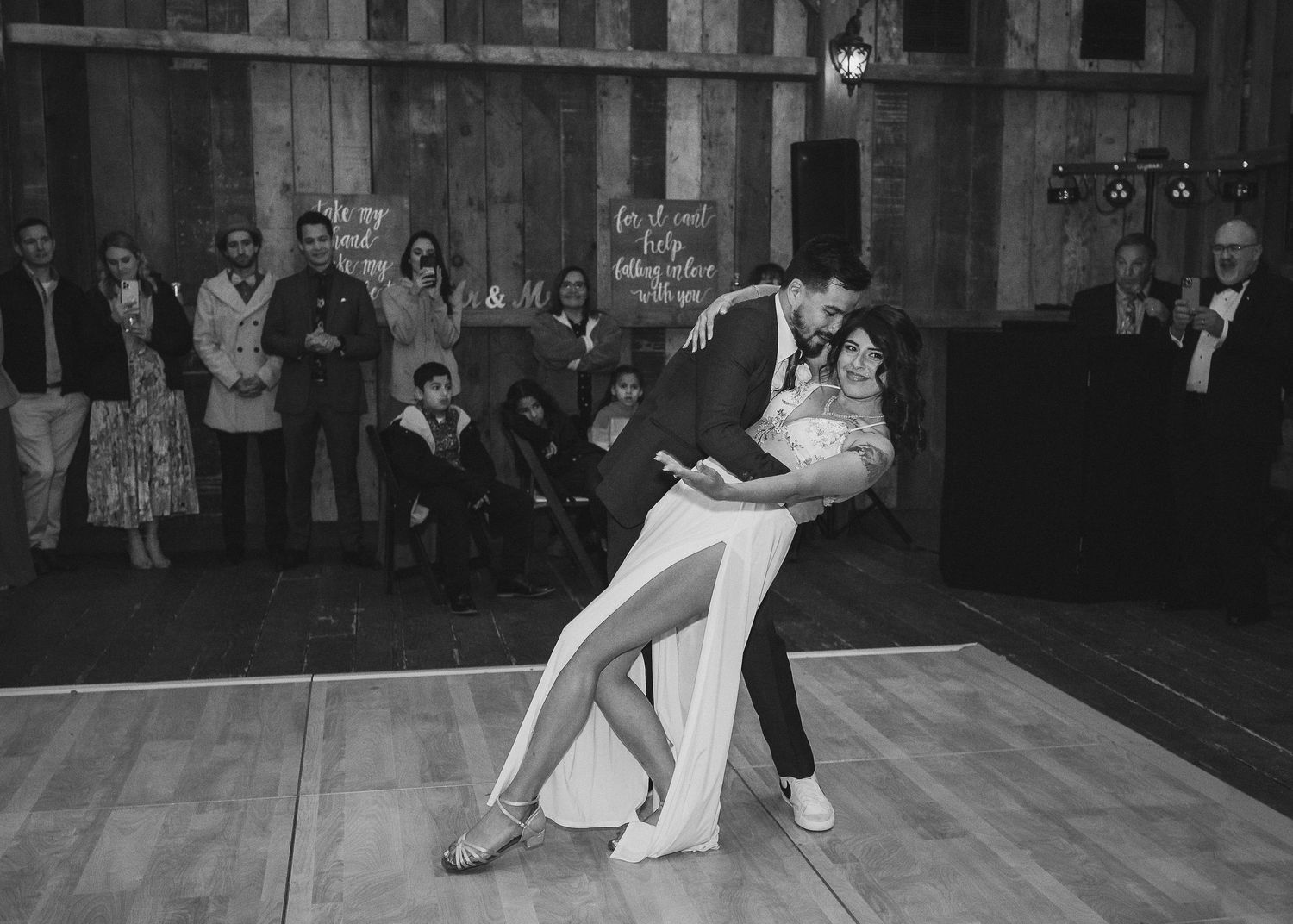 A couple performs an elegant dance move during their first dance in a rustic barn venue.