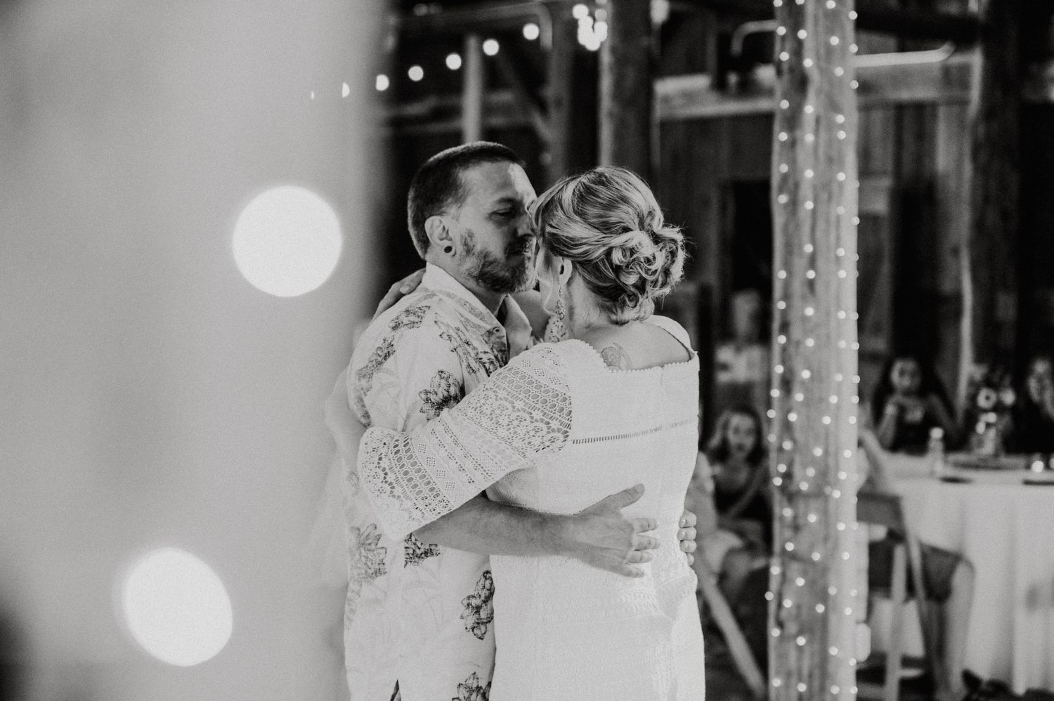 Black and white photo of a couple dancing together at a wedding reception with string lights in the background.