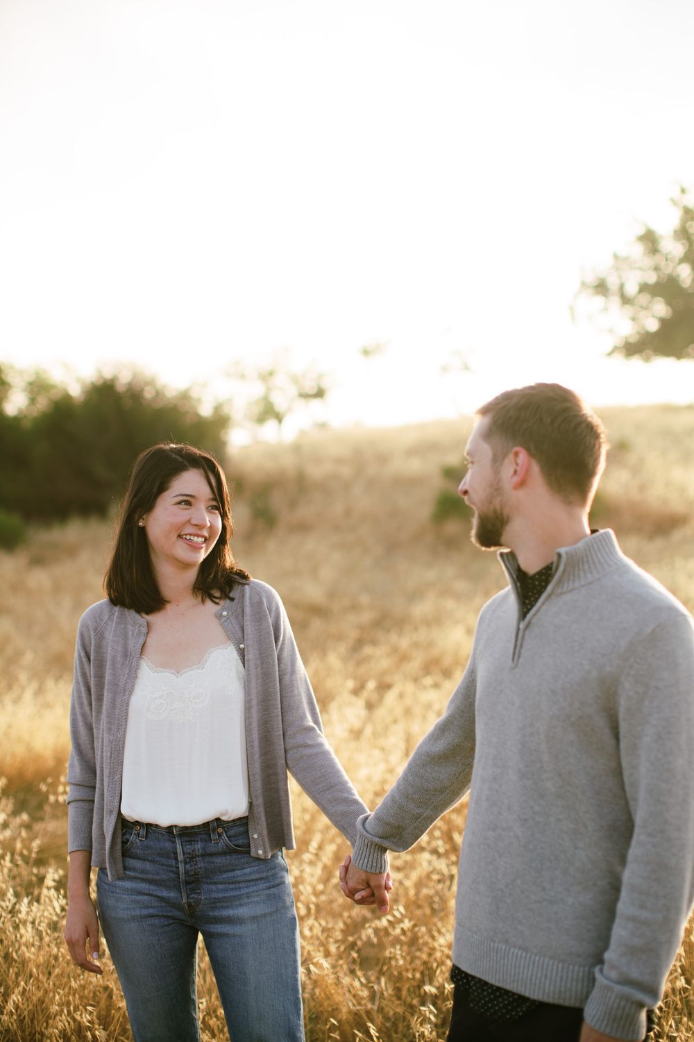 Couple holding hands and smiling in golden field during sunset.