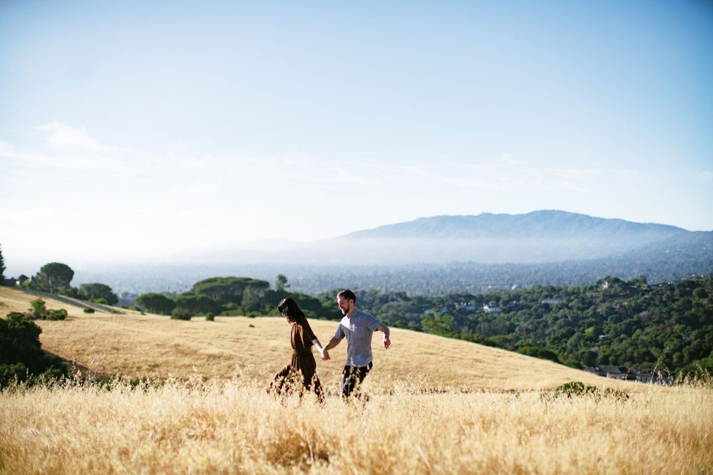 Couple walking through golden hillside with mountain vista in background.