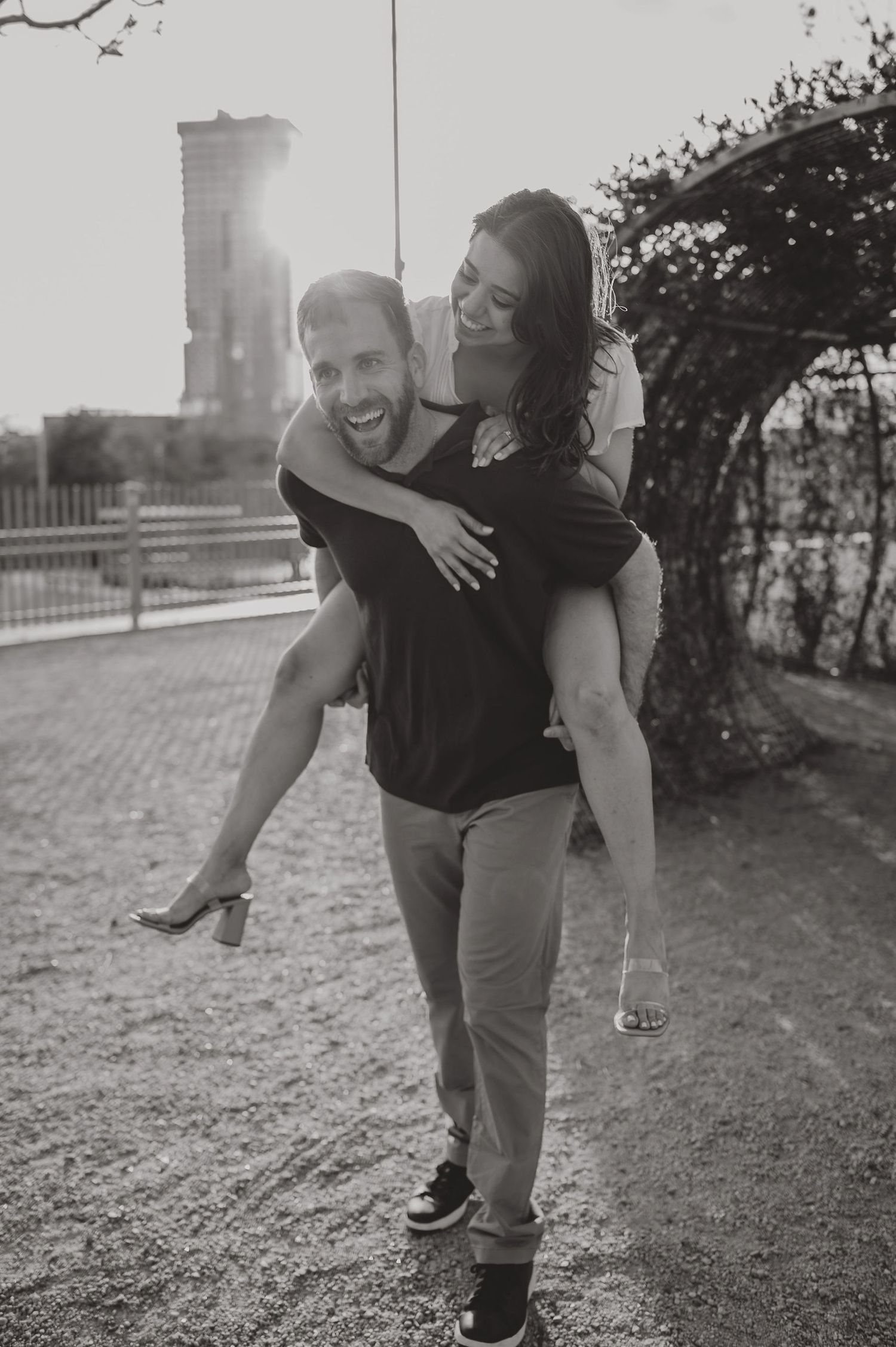 A piggyback ride moment captured between a couple outdoors with a tower in the background.