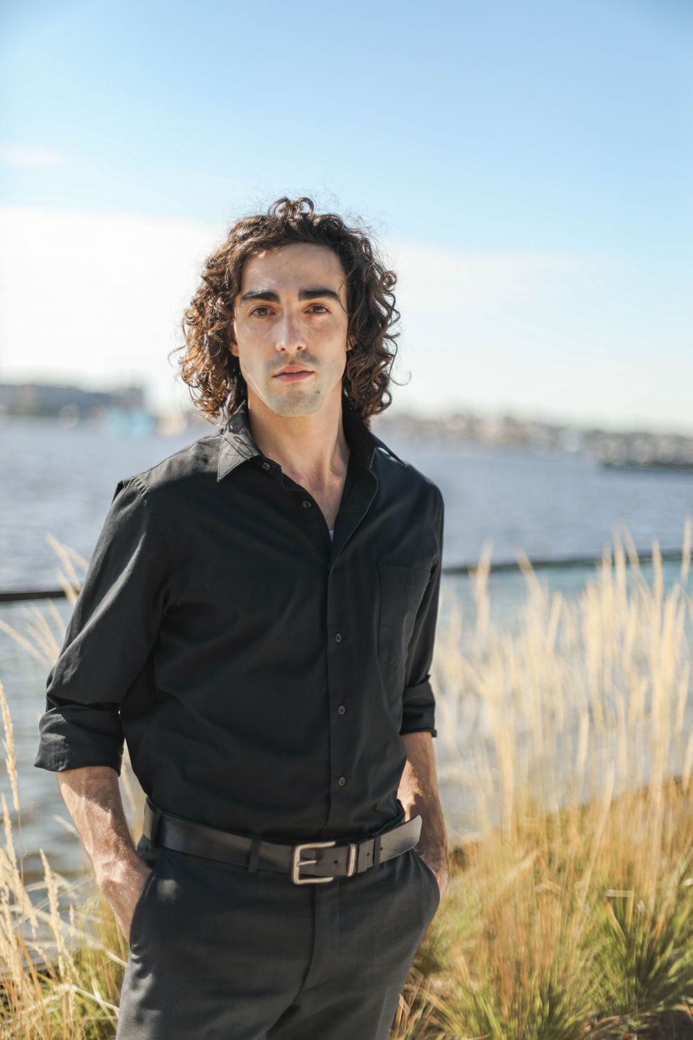 Editorial style image of a young man in a black button down near water and tall grasses