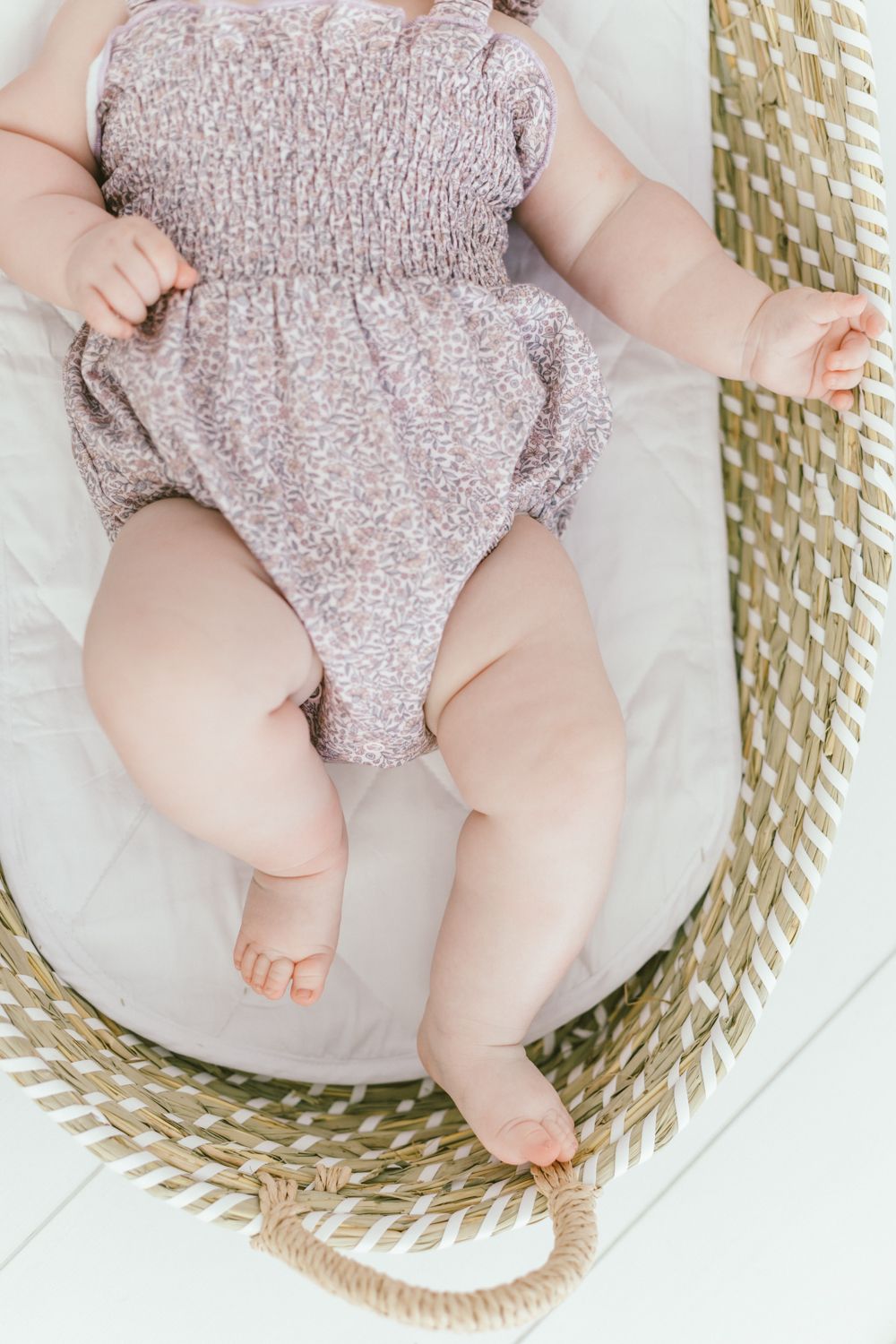 Close-up view of baby wearing smocked pink romper lying in woven basket.