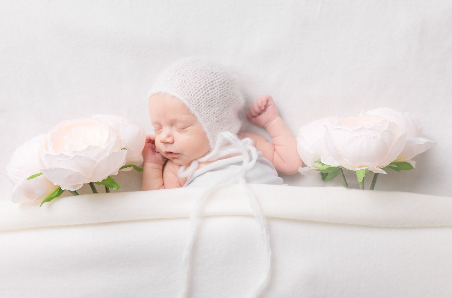 Newborn baby sleeping peacefully between pink roses on white soft fabric.