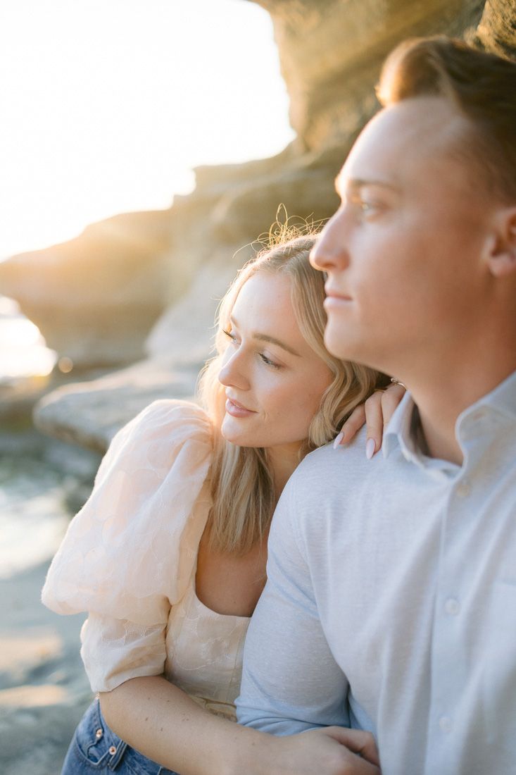 Romantic couple embraces while watching sunset on beach with golden light filtering through.