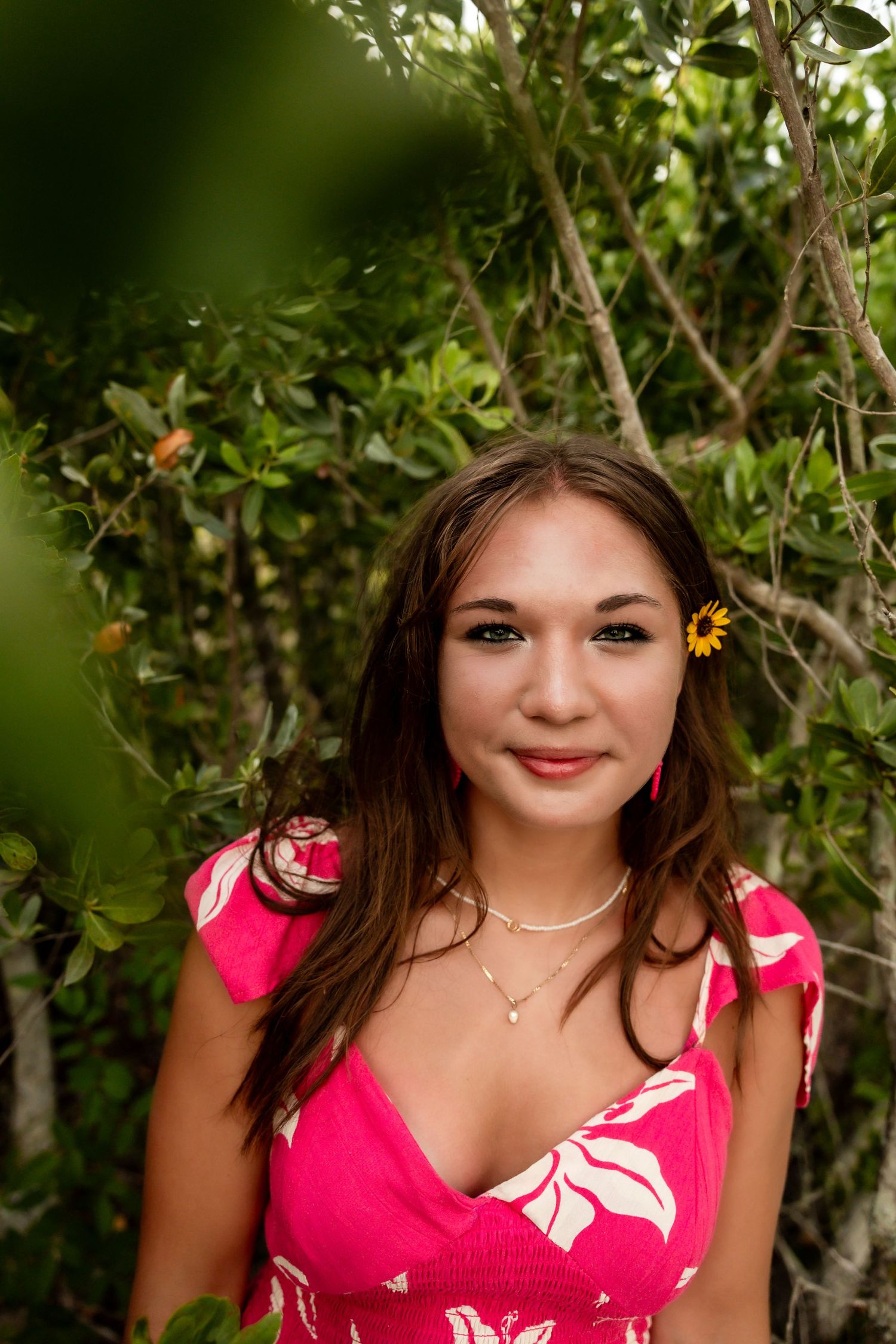 Young woman in pink floral dress smiling among lush green tropical mangrove trees.