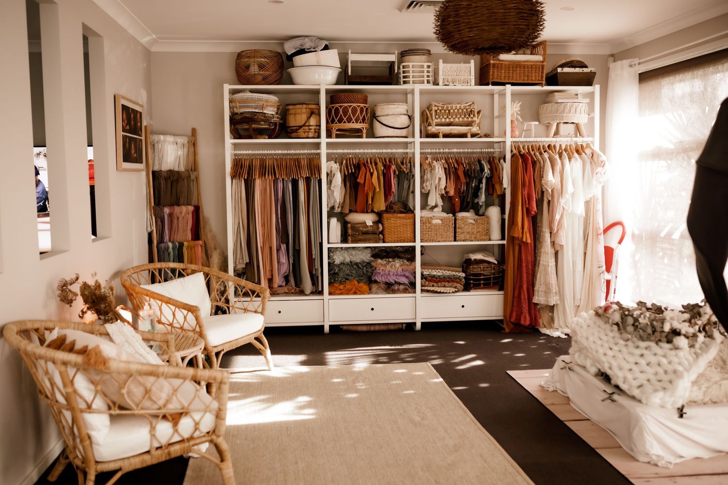 Bright, organized walk-in closet with white shelving, wicker accents, and natural sunlight streaming in.