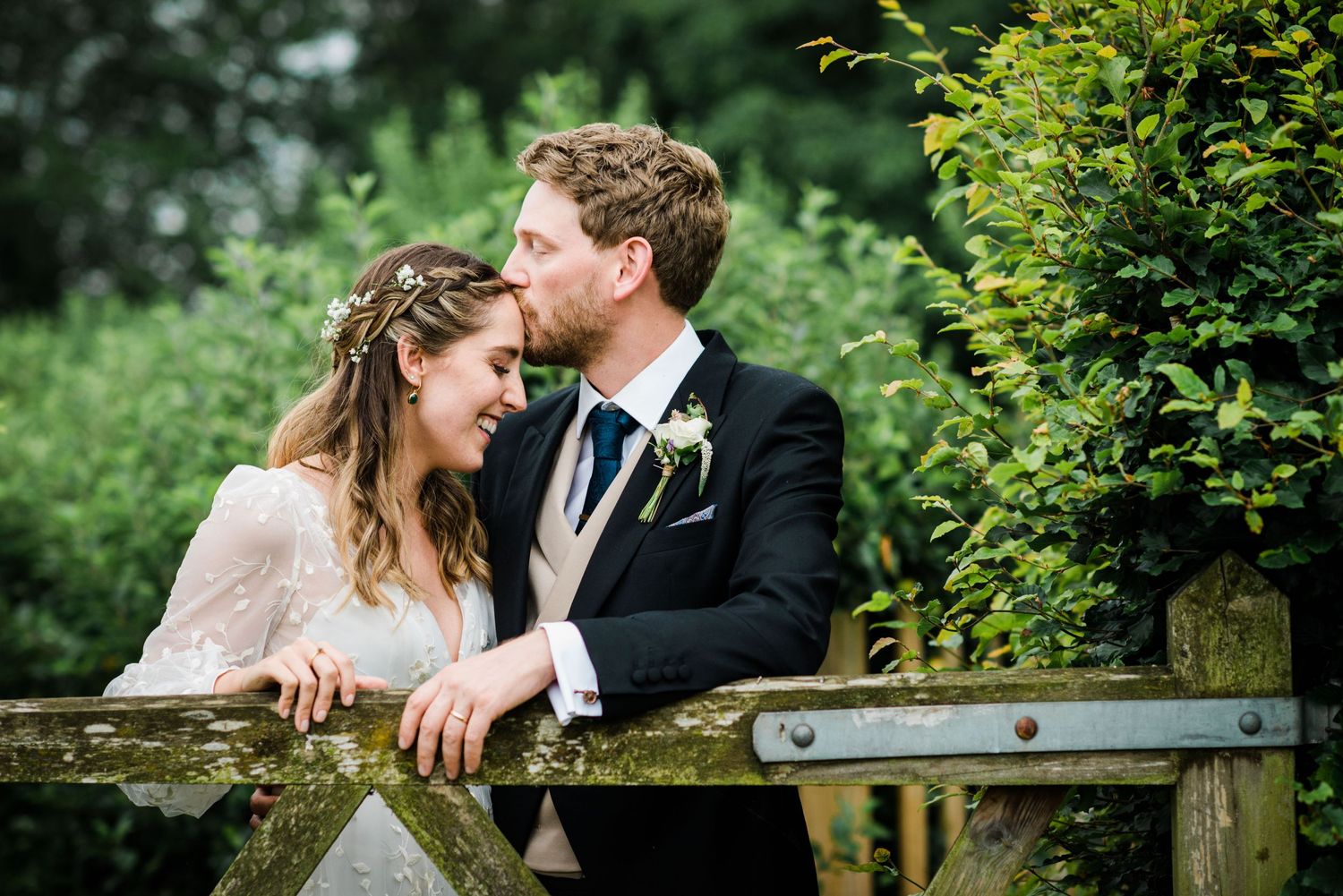 Groom kisses bride on the forehead as they share a relaxed moment away from the wedding party.