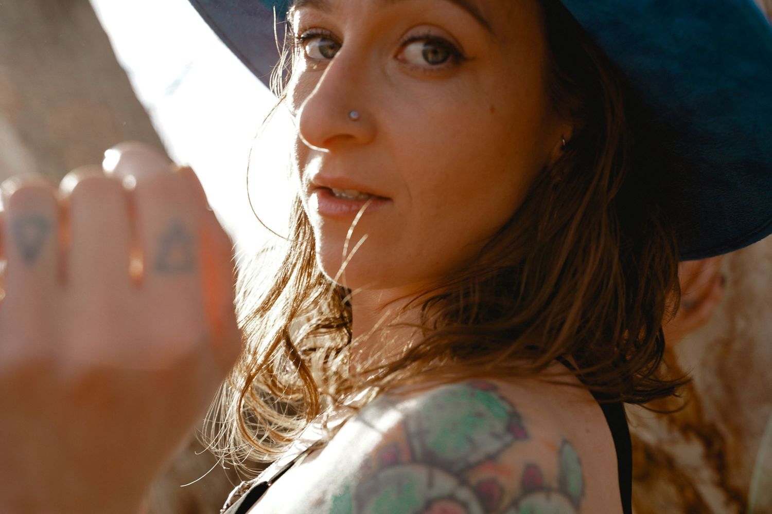 Close up portrait of woman in sunlight wearing black hat with visible tattoos.