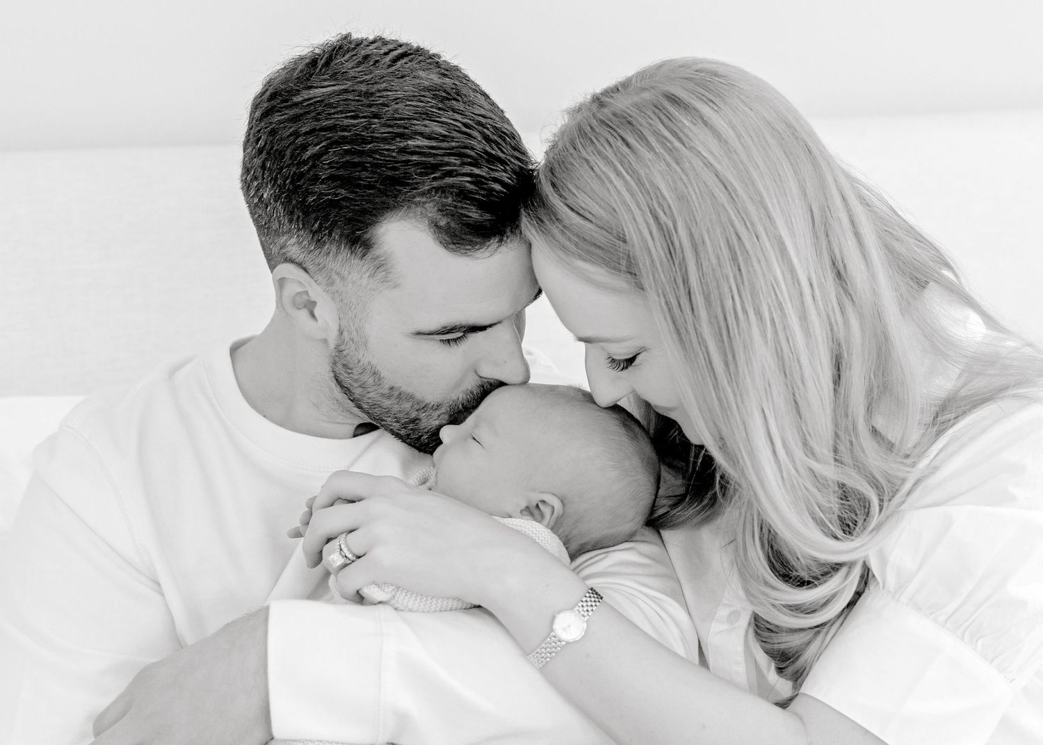 Black and white portrait of tender family moment in minimalist setting.