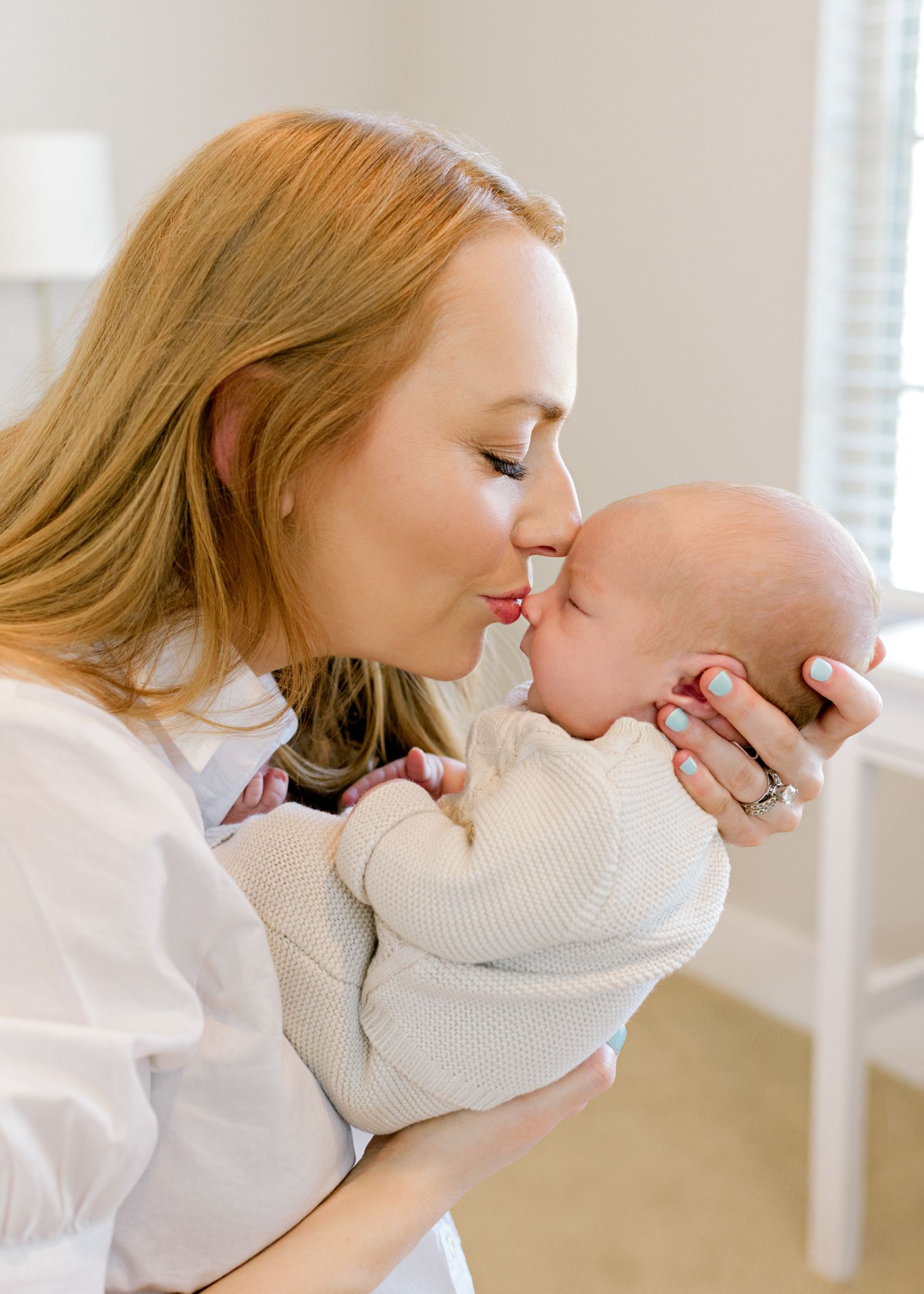 Intimate newborn portrait in natural light showing gentle maternal bonding moment in white clothing.